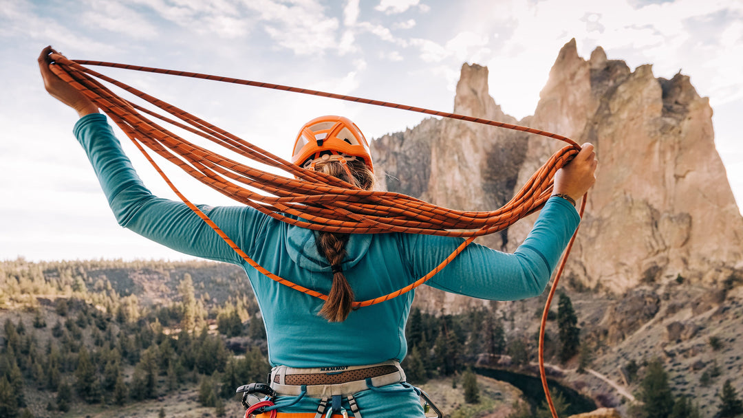 A woman coils a rock climbing rope while looking at the peaks of Smith Rock State Park