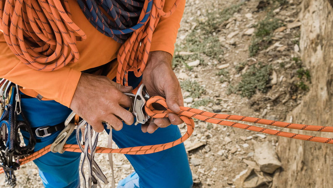 A rock climber sets up a belay device with a climbing rope