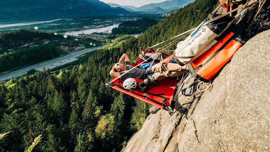 A climber relaxes on a portaledge that is suspended high above the ground on The Stawamus Chief