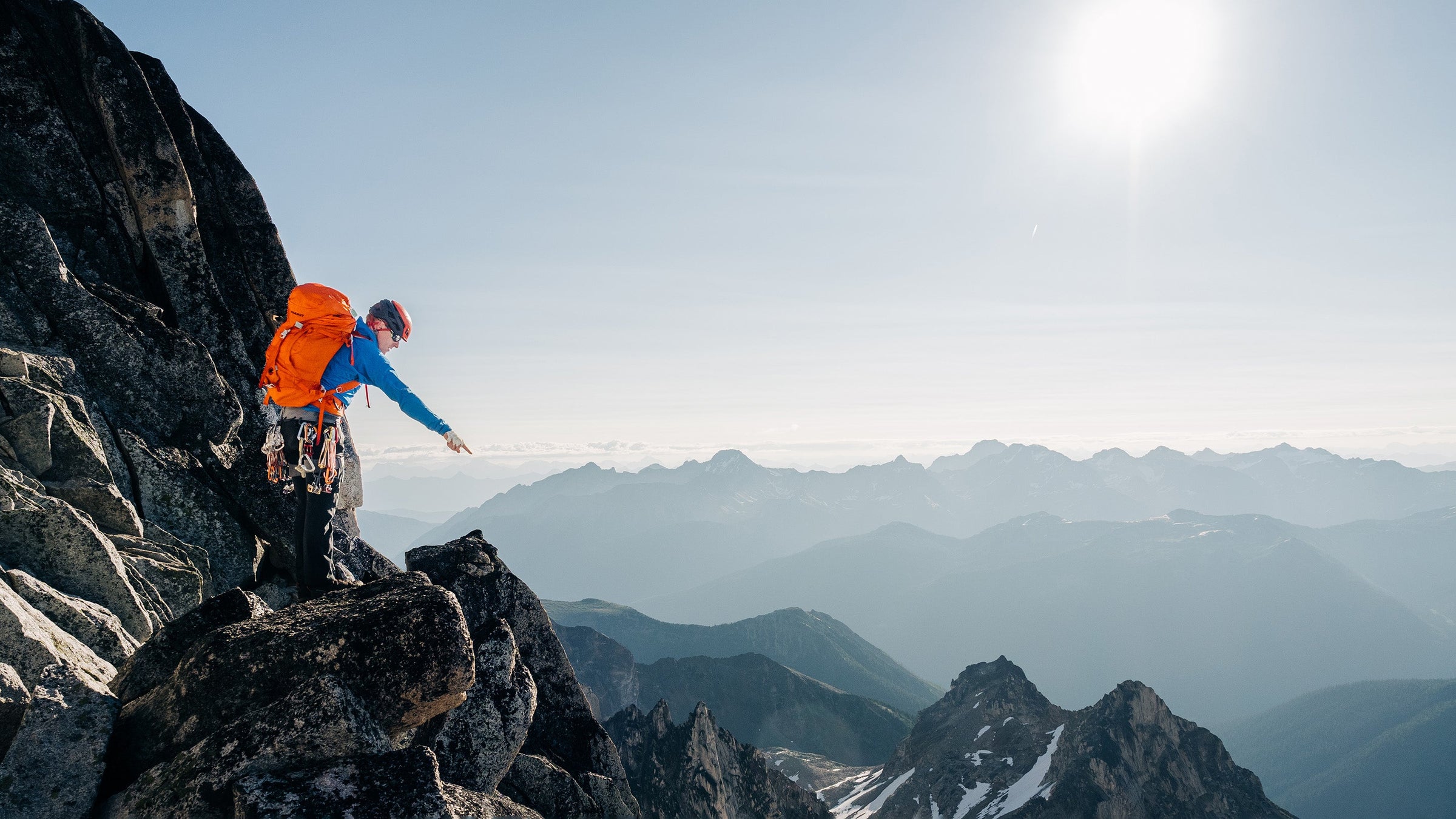 A male alpine climber points out at a view from a high mountain ridge on Bugaboo Spire