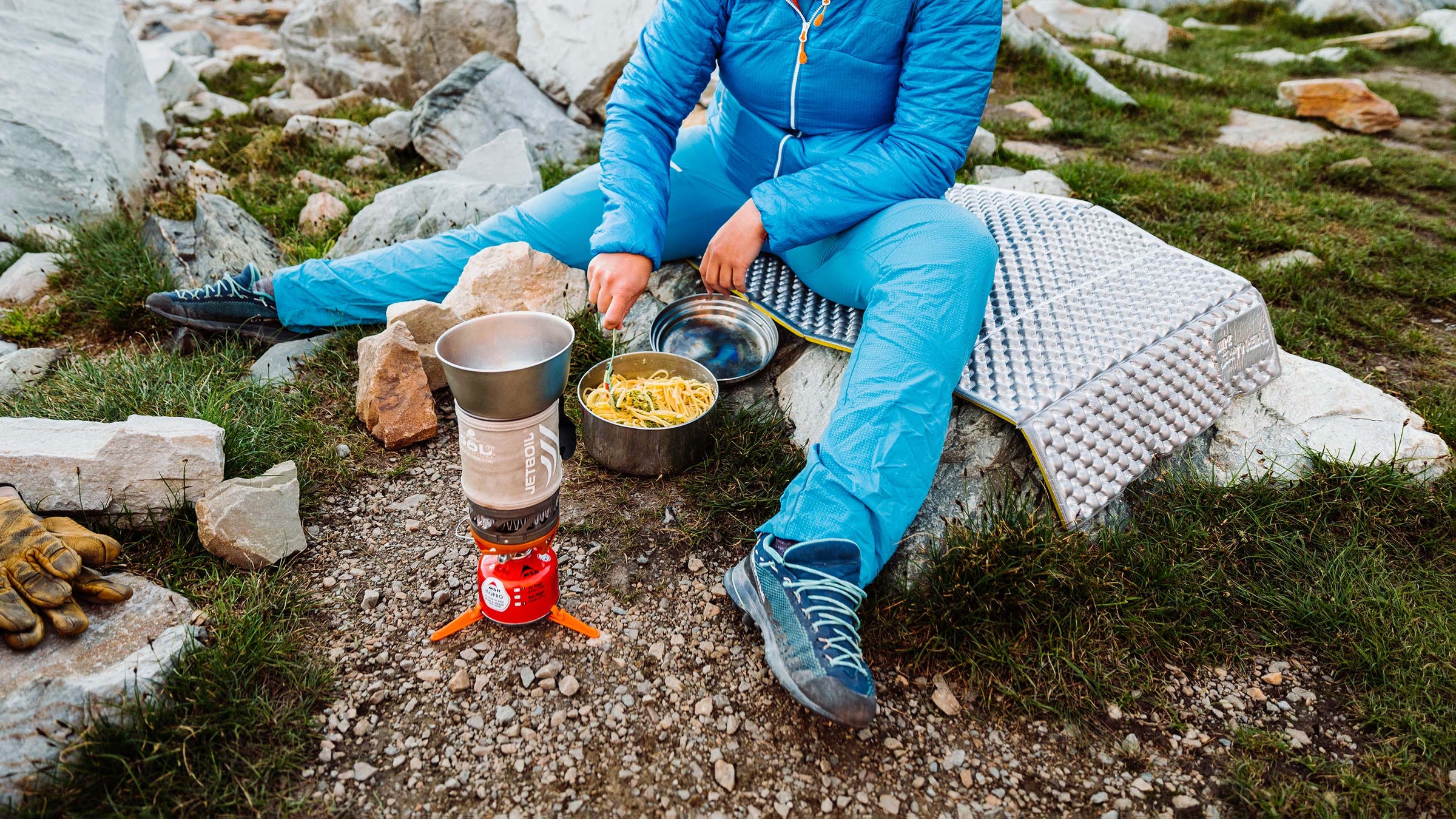 Close up of a woman cooking pasta on a jetbil camping stove while climbing in the mountains