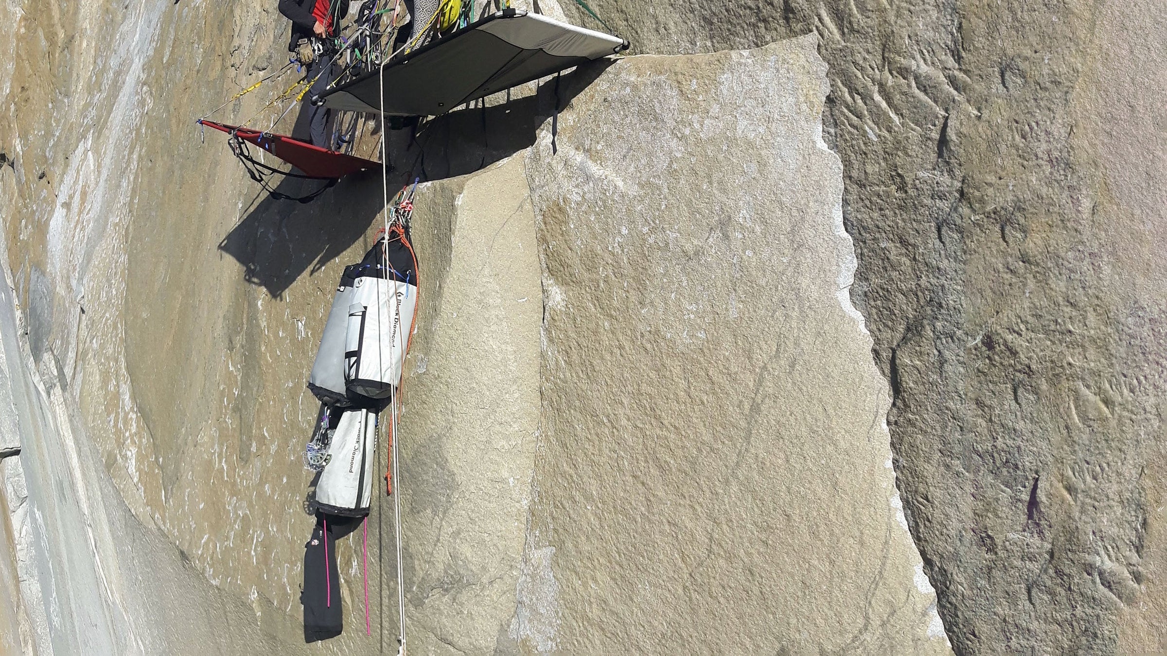 Haul bags are suspended from a rope on the side of a tall rock face in Yosemite National Park