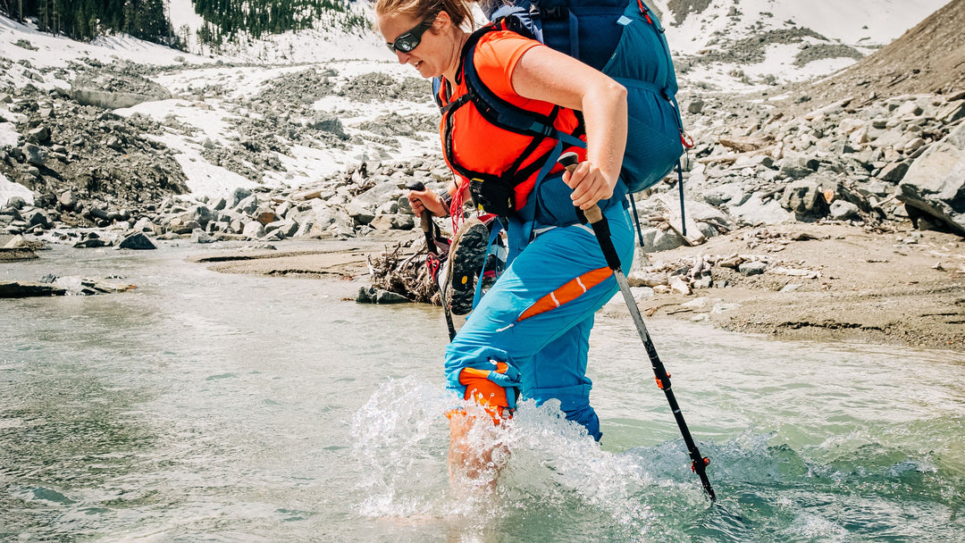 A woman crosses a river using hiking poles to keep her balance