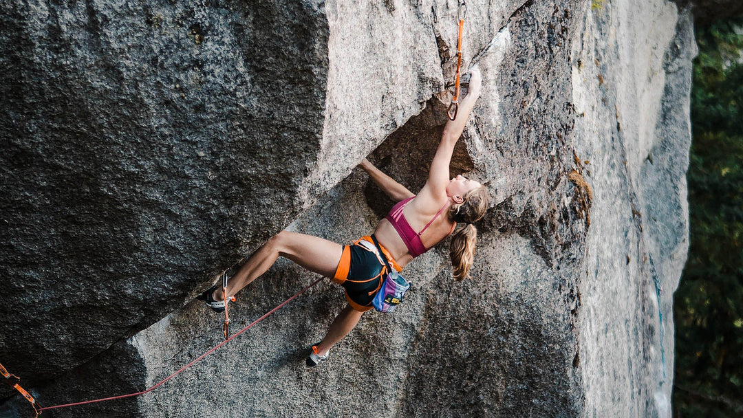 A woman wearing a harness rock climbs up an overhung sport climb