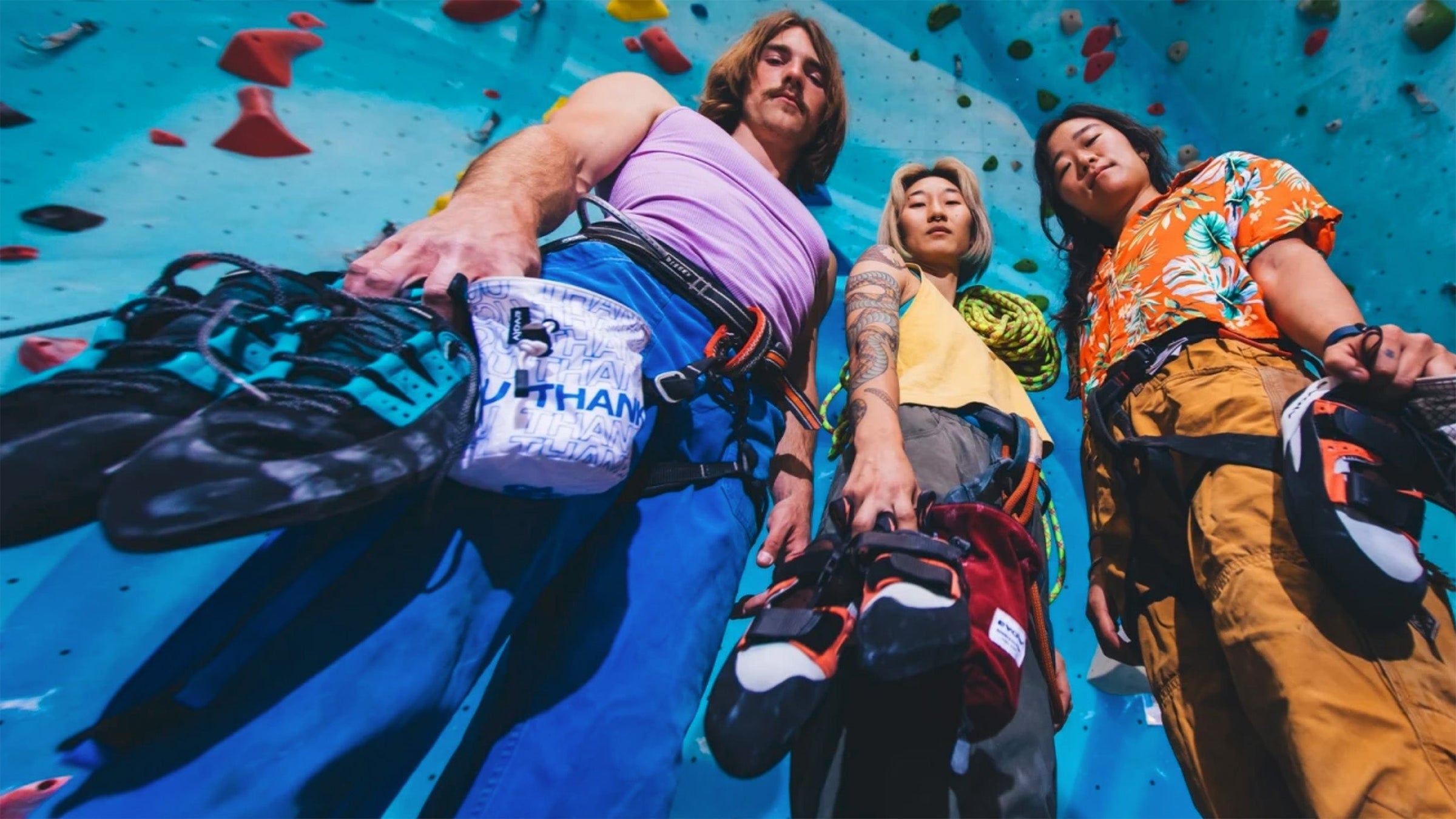 3 people holding Evolve rock climbing shoes in a gym