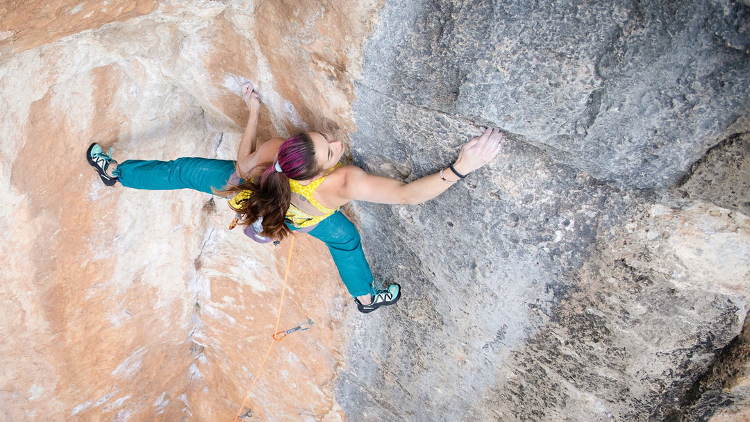 A female rock climber ascends a tall sport climb wearing a pair of climbing shoes