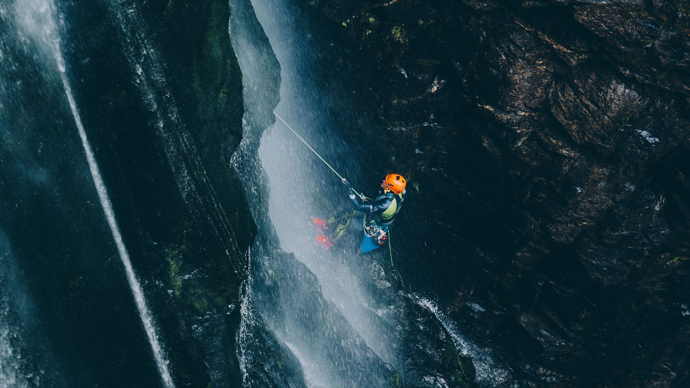 A Canyoner rappels down a static rope beside a waterfall in a canyon