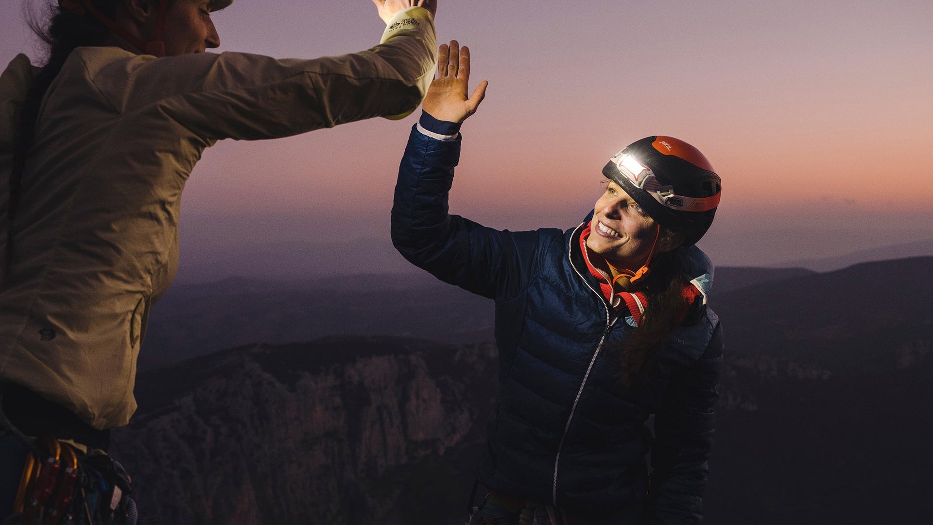 A woman wearing a headlamp high fives her rock climbing partner after summiting