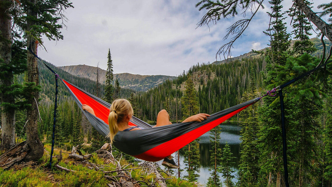 A woman relaxes in a hammock setup by a forested lake while backcountry camping